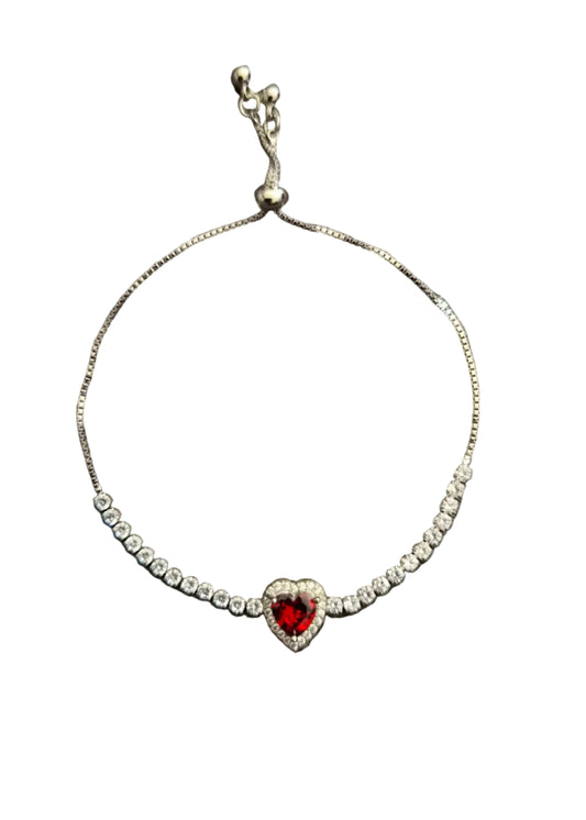 A delicate silver chain bracelet featuring a central heart-shaped red gemstone surrounded by small clear stones.