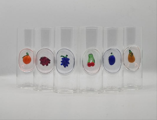 Set of clear glass shot glasses with glass fruit designs on a white background